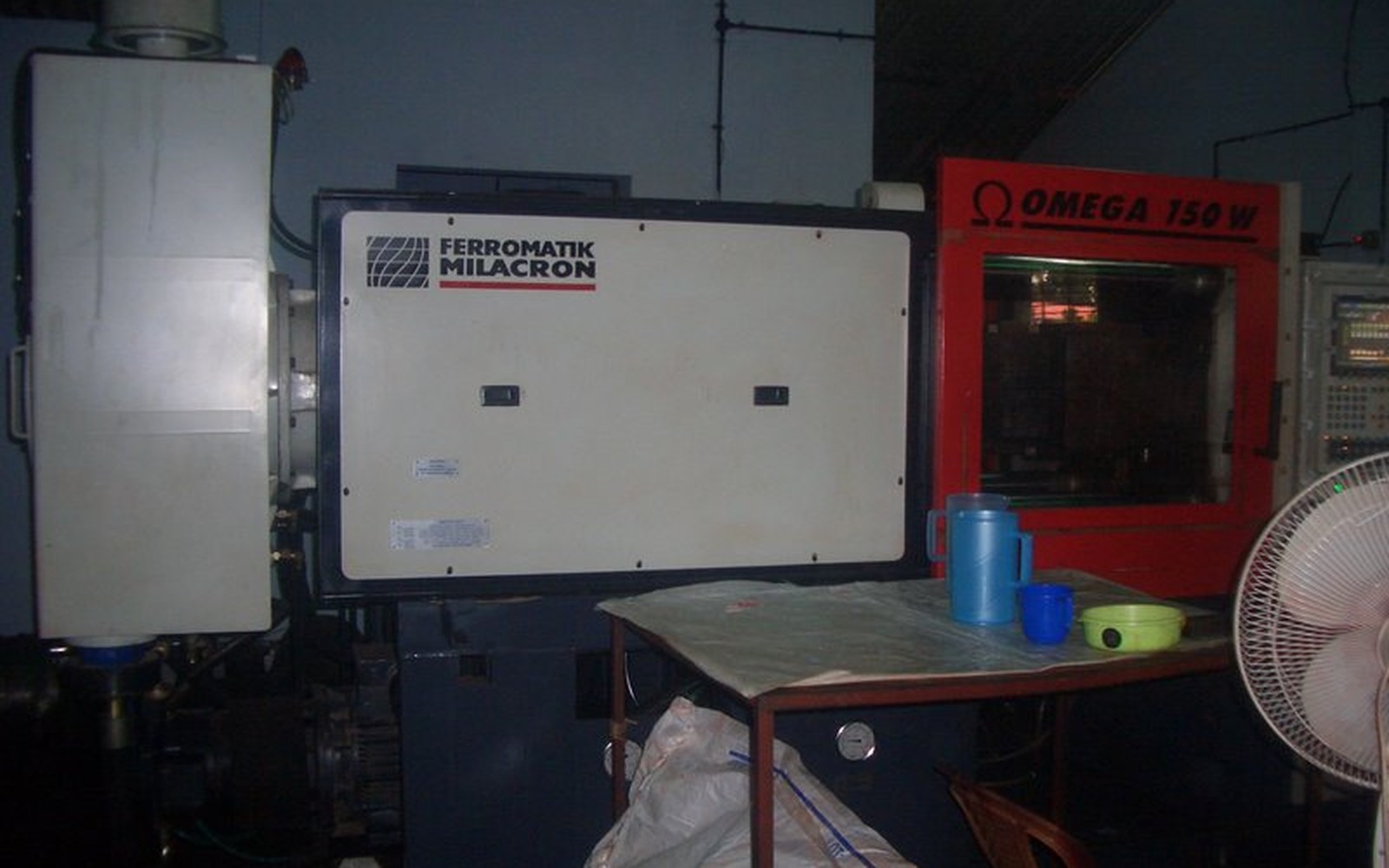 Ferromatik Milacron injection moulding machine beside a red Omega 150 W unit in a factory